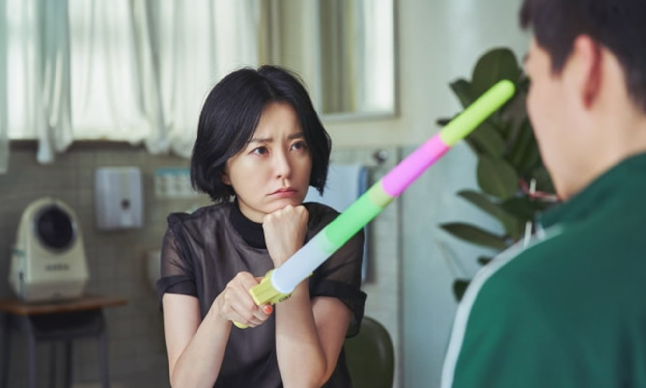 넷플릭스 《보건교사 안은영》의 한 장면 — 보건실에서 검은 상의를 입은 안은영이 무지개색 장난감 칼을 두 손으로 치켜든 채 긴장한 표정으로 맞은편의 인물을 겨누고 있다
